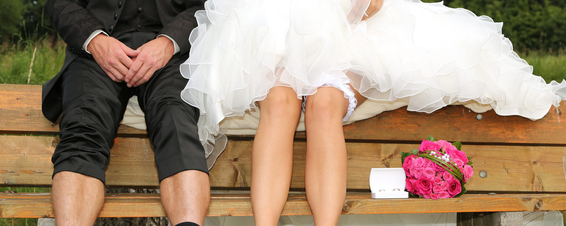Ein Brautpaar sitzt auf der Lehne einer Bank wobei ihre Gesichter nicht zu sehen sind