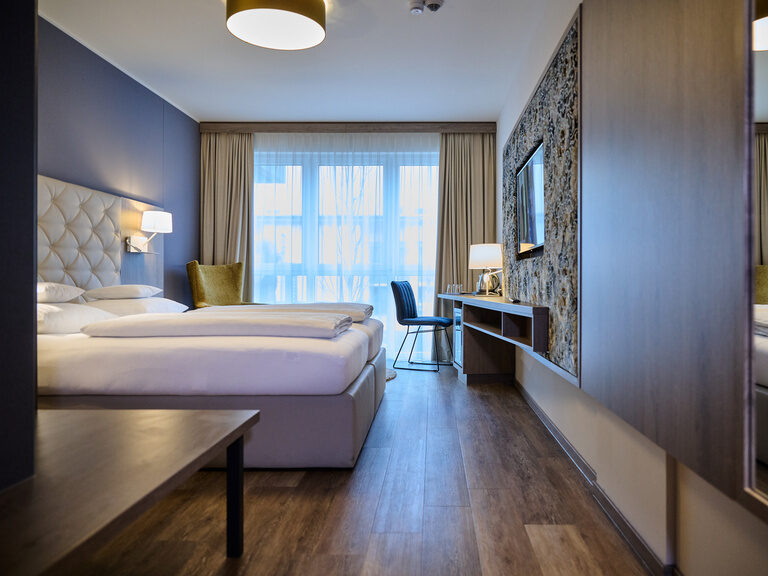 Auf dem Bild ist fast das gesamte Premium Zimmer mit dem großen Doppelbett und dem kleinen Schreibtisch zu sehen