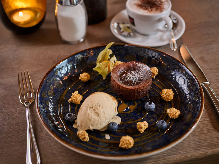 Ein Teller mit lauwarmen Schokokuchen der mit Salz und Karamell getoppt wird steht auf einem Tisch